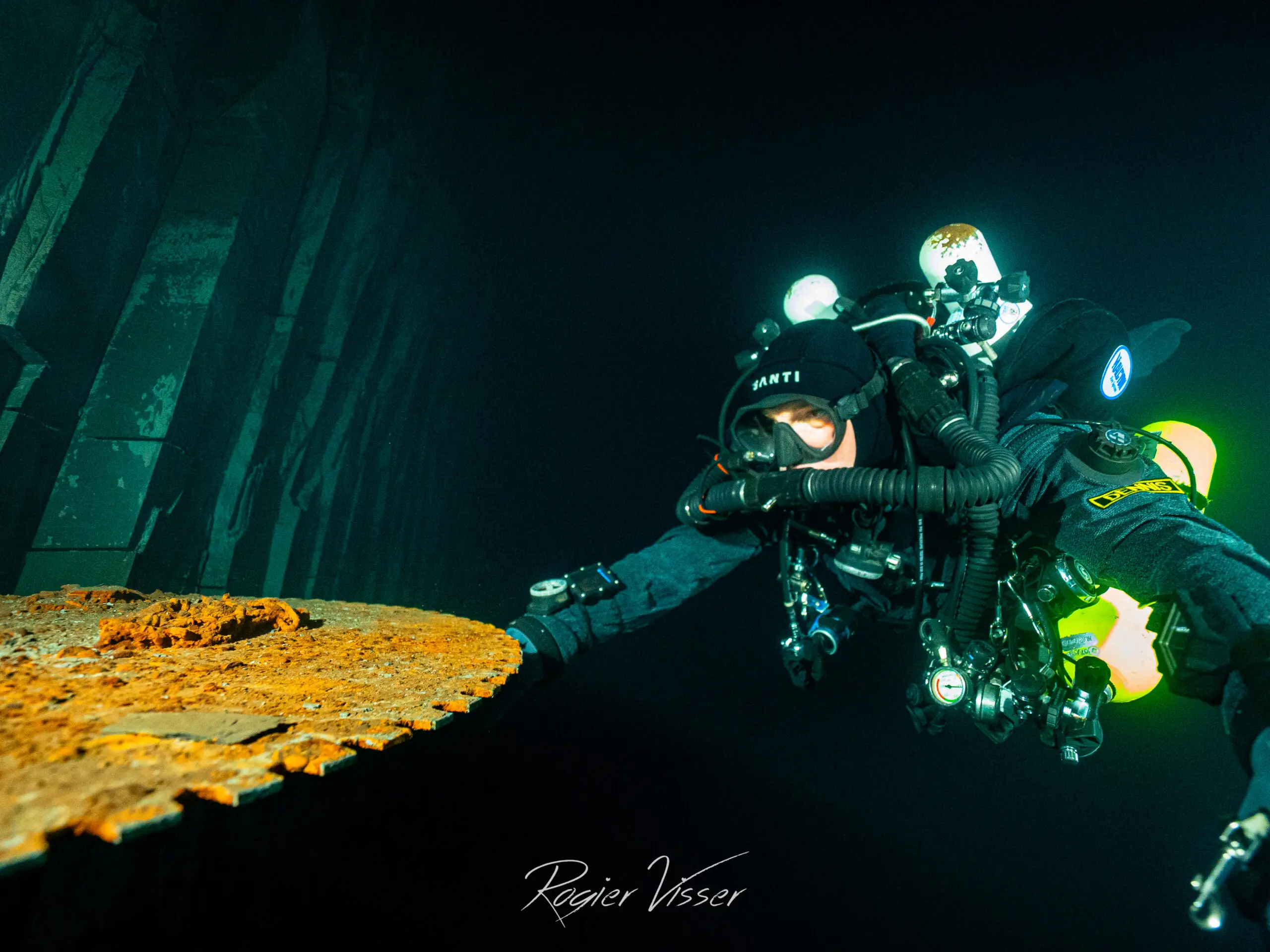 Duiker met rebreather naast een verroeste ijzeren plaat diep in een ondergelopen mijn
